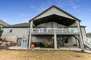 Back of property featuring a patio area, a hot tub, a deck, and a lawn