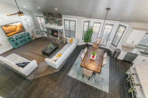Living area featuring a stone fireplace, ceiling fan, wood finish floors, vaulted ceiling, and a chandelier