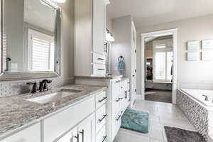 Full bath featuring two vanities, tiled tub, and light tile patterned floors