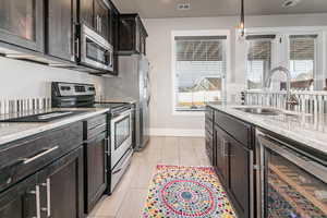Kitchen with stainless steel appliances, beverage cooler, light stone countertops, and decorative light fixtures