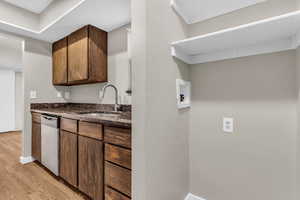 Kitchen with dark stone counters, light wood finished floors, dishwasher, and dark wood finish cabinets