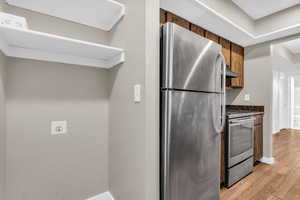 Kitchen featuring stainless steel appliances, light wood-type flooring, wood finish cabinetry, and dark stone counters