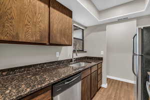 Kitchen with stainless steel appliances, dark stone countertops, light wood-style floors, dark wood finish cabinetry, and a tray ceiling