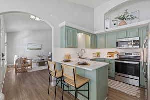 Kitchen featuring green cabinetry, stainless steel appliances, a breakfast bar, a peninsula, and dark wood finished floors