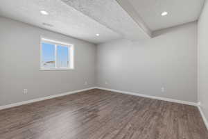 Empty room with wood finished floors, a textured ceiling, and recessed lighting