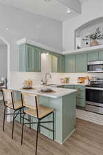 Kitchen with green cabinetry, a peninsula, stainless steel appliances, and a kitchen breakfast bar