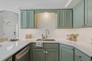 Kitchen with green cabinetry, stainless steel dishwasher, light stone countertops, and tasteful backsplash