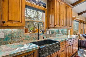 Kitchen featuring beamed ceiling, wood finish cabinets, tasteful backsplash, and light stone counters