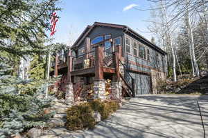 View of front of home with driveway, an attached garage, a deck, and stone siding