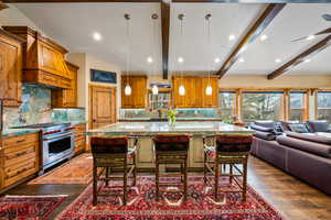 Kitchen featuring wood finish cabinets, light stone countertops, a large island, pendant lighting, and vaulted ceiling with beams
