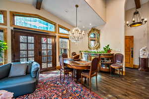 Dining space with a chandelier, french doors, wood finished floors, healthy amount of natural light, and vaulted ceiling