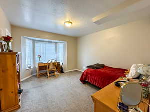 Bedroom with an office area, a textured ceiling, and light carpet