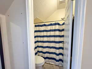 Bathroom featuring a shower with shower curtain, a textured wall, and lofted ceiling