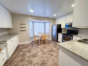 Kitchen with light stone countertops, stainless steel appliances, white cabinetry, and recessed lighting
