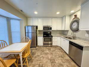 Kitchen with stainless steel appliances, white cabinetry, recessed lighting, stone finish flooring, and light stone counters