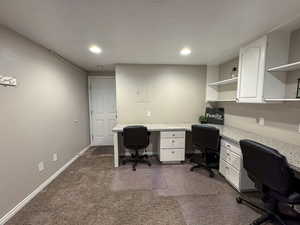 Office space with dark colored carpet, recessed lighting, built in desk.