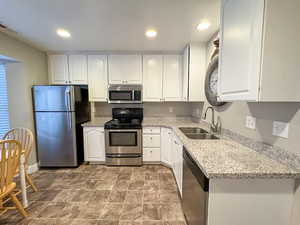 Kitchen with stainless steel appliances, light stone countertops, white cabinetry, recessed lighting, and stone finish floors