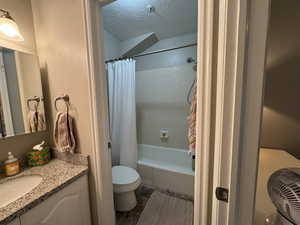Full bath with a textured ceiling, vanity, and shower / bathtub combination with curtain