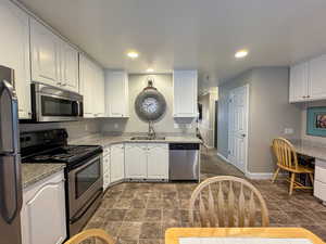 Kitchen with stainless steel appliances, white cabinetry, recessed lighting, and light stone counters
