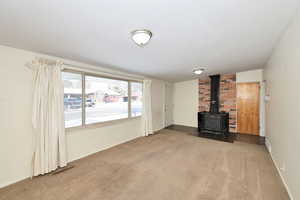 Unfurnished living room featuring a wood stove and carpet floors