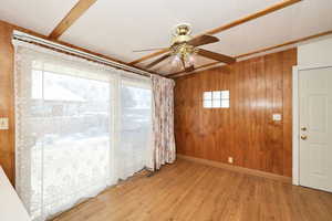 Spare room featuring wood walls, ceiling fan, and light wood finished floors