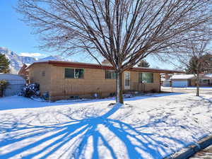 Snow covered house featuring brick siding, an outdoor structure, and a mountain view