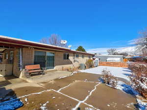 Snow covered rear of property featuring brick siding, a patio, and a shed