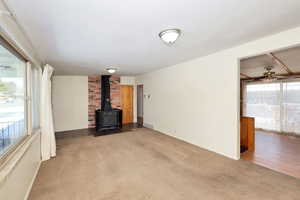 Unfurnished living room featuring carpet flooring, a wood stove, and a ceiling fan