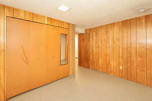 Unfurnished bedroom with concrete floors, wooden walls, a textured ceiling, and a closet