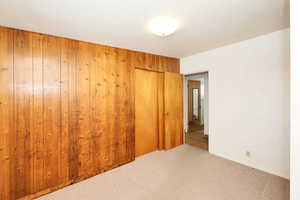 Unfurnished bedroom with carpet, a closet, and wood walls