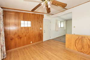 Entrance foyer with ceiling fan, wooden walls, light wood finished floors, and lofted ceiling with beams