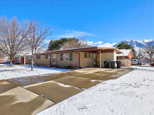 Snow covered property featuring a carport, brick siding, a mountain view, and driveway