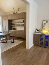 Bar featuring wine cooler, modern cabinets, light wood finished floors, wood finish cabinetry, and vaulted ceiling