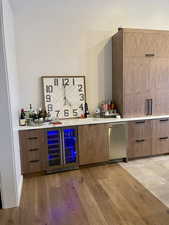Indoor bar featuring modern cabinets, beverage cooler, light wood finished floors, and light stone countertops