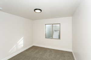 Empty room featuring baseboards and dark colored carpet