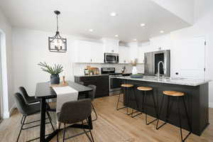 Dual tone kitchen featuring stainless steel appliances, hanging light fixtures, light wood-type flooring, a center island with sink, and a kitchen breakfast bar