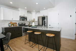 Two tone kitchen with a breakfast bar, stainless steel appliances, light wood finished floors, light stone counters, and an island with sink