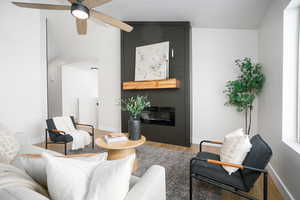 Living area featuring vaulted ceiling, wood finished floors, a large fireplace, and ceiling fan