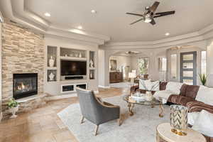 Living area with ceiling fan, built in shelves, a tile fireplace, arched walkways, and stone tile floors
