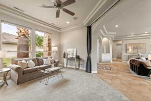 Living area featuring a tray ceiling, a ceiling fan, stone tile flooring, arched walkways, and recessed lighting