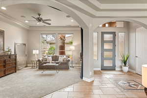 Foyer featuring arched walkways, a ceiling fan, light tile patterned flooring, a tray ceiling, and light colored carpet