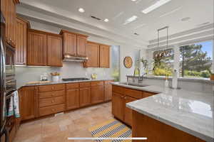 Kitchen with wood finish cabinets, light stone counters, pendant lighting, a tray ceiling, and stainless steel appliances
