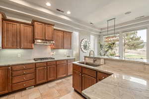 Kitchen featuring wood finish cabinetry, light stone counters, decorative light fixtures, backsplash, and a tray ceiling