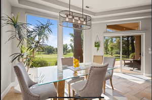 Dining room with view of golf course, healthy amount of natural light, a raised ceiling, suspended lighting, and stone tile flooring