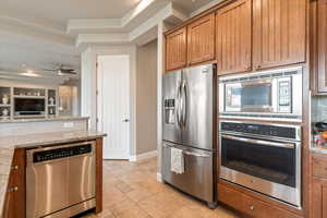 Kitchen with stainless steel appliances, light stone countertops, wood finish cabinetry, a ceiling fan, and a raised ceiling
