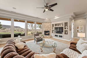 Living room with a ceiling fan, built in features, a raised ceiling, a stone fireplace, and light tile patterned floors