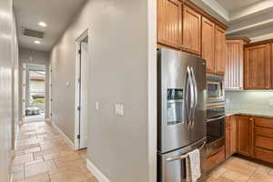 Kitchen featuring stainless steel appliances, wood finish cabinets, recessed lighting, light stone counters, and tasteful backsplash