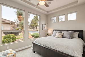 Bedroom featuring light carpet, a tray ceiling, and ceiling fan