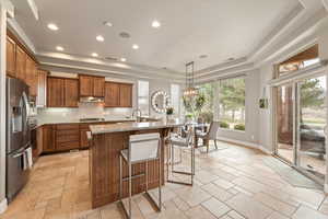 Kitchen featuring a tray ceiling, a breakfast bar area, wood finish cabinets, a center island with sink, and stainless steel appliances