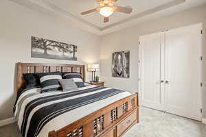 Bedroom featuring light colored carpet, a tray ceiling, and ceiling fan